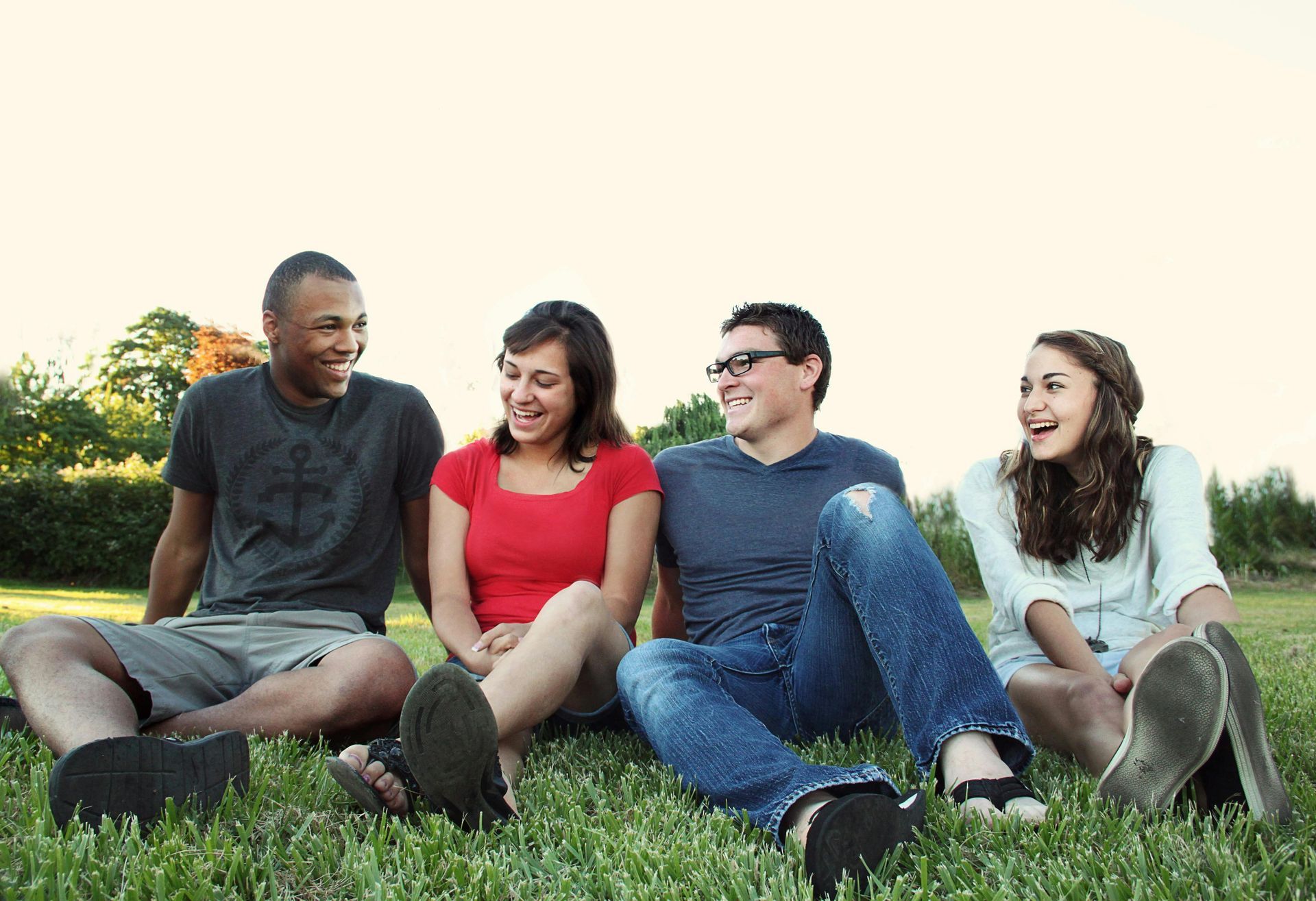A group of young people are sitting on the grass and laughing.