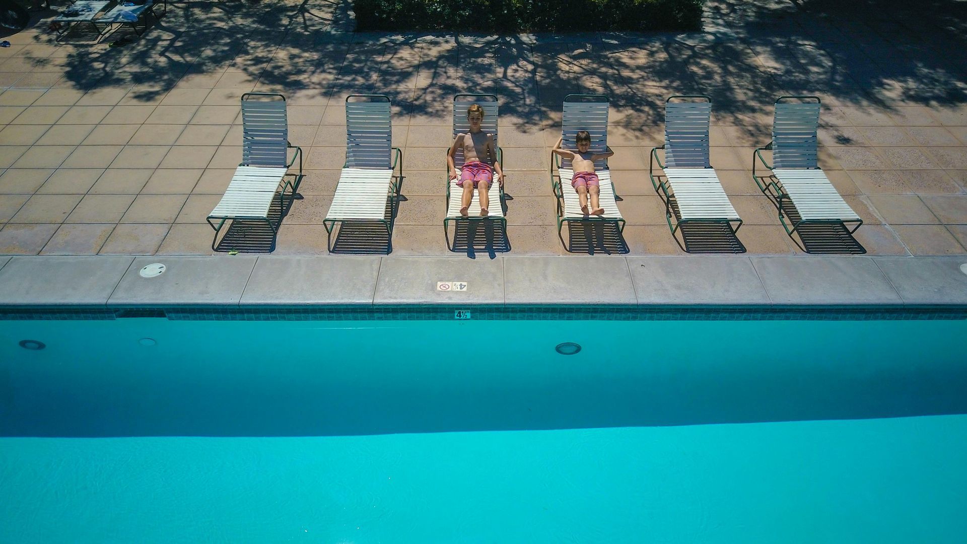 A woman is sitting on a lounge chair next to a swimming pool.