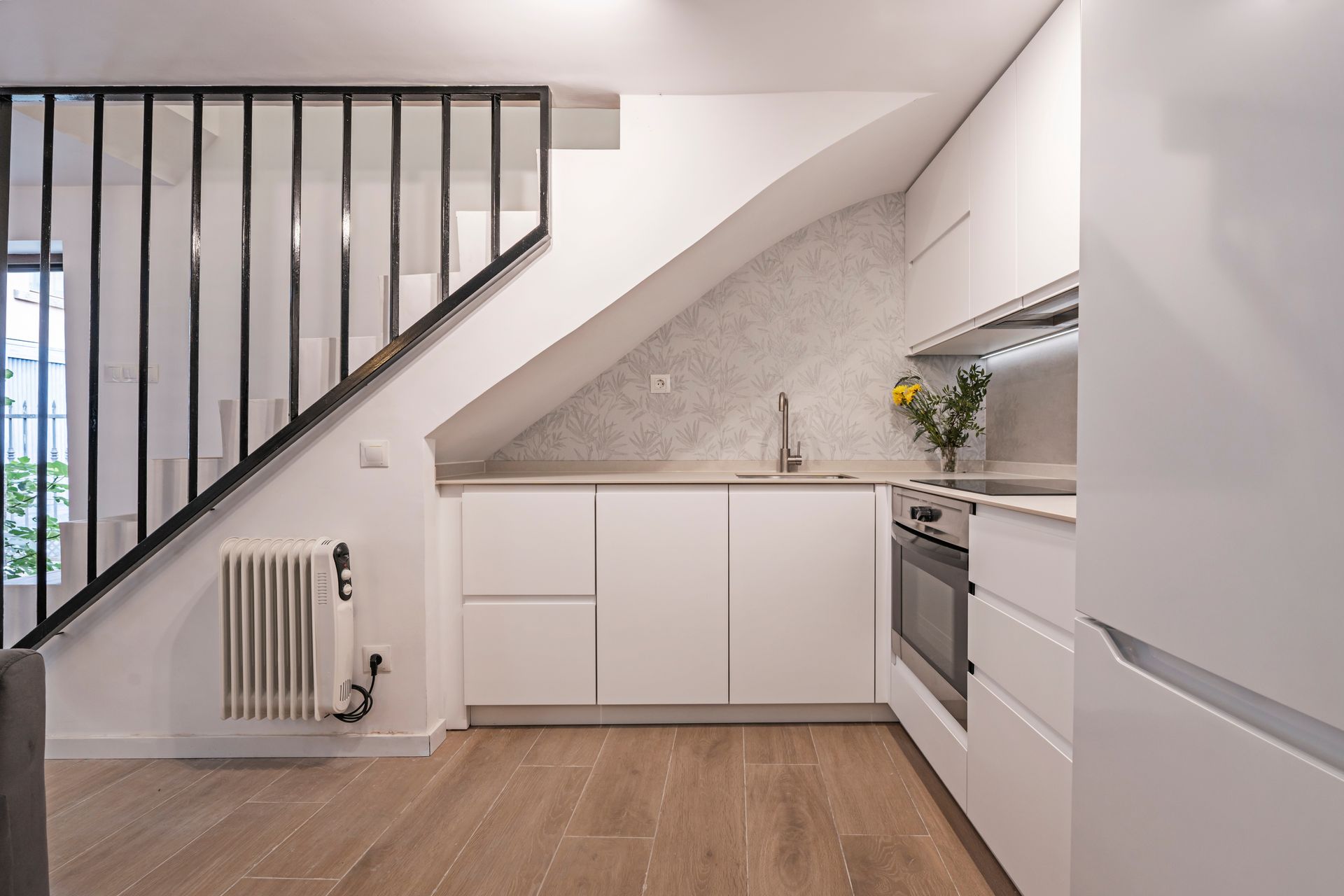 A modern kitchen featuring white cabinets, wood-look floors, and an under-stairs counter area with a radiator.