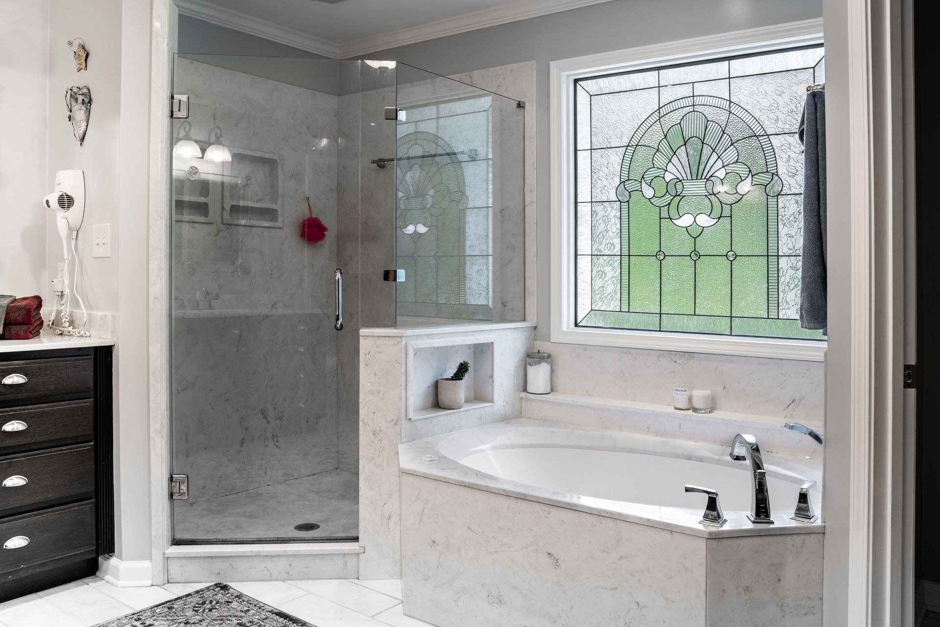 A modern bathroom featuring a white marble bathtub, a glass-enclosed shower, and a large decorative stained-glass window.