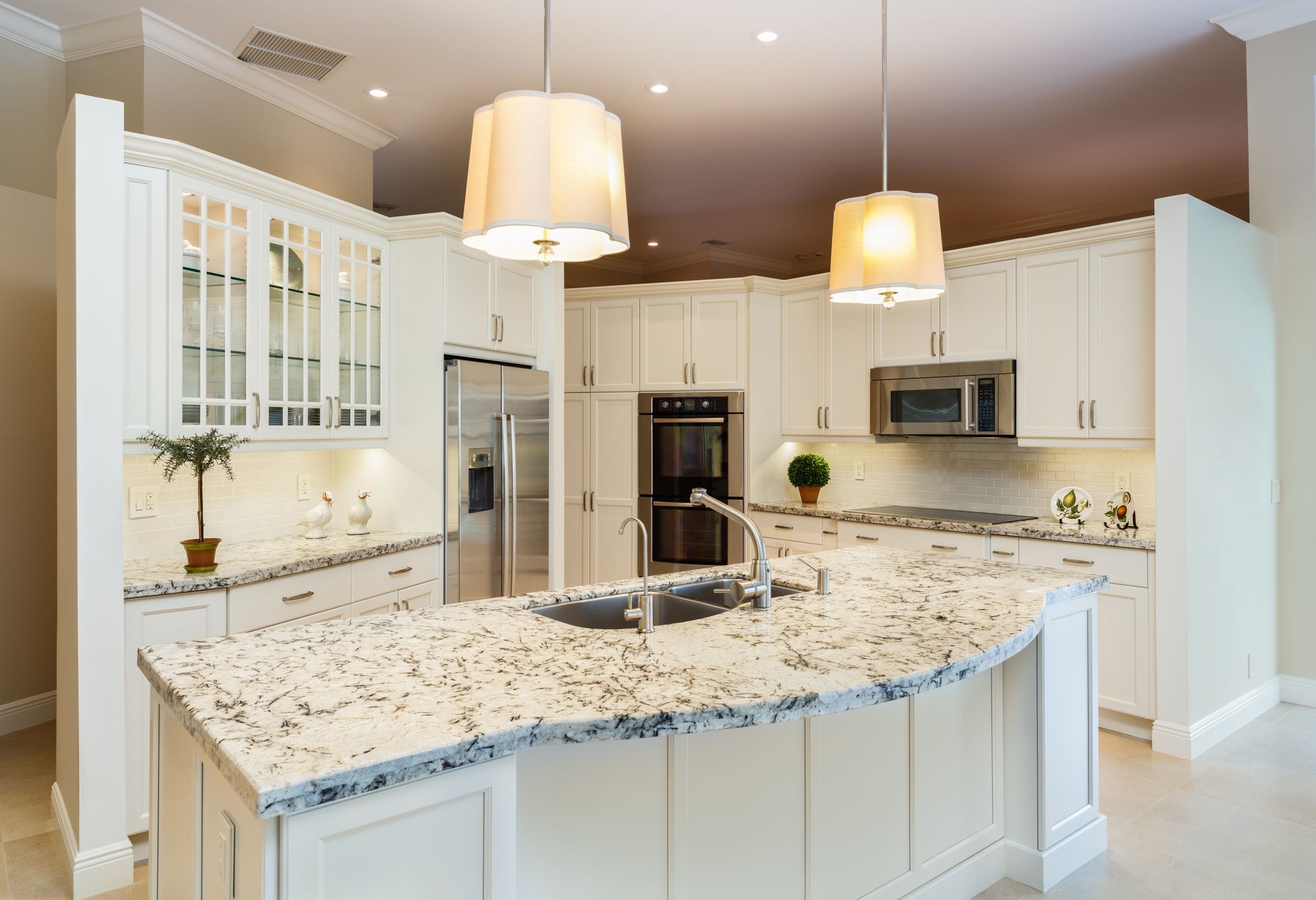 A bright, modern kitchen featuring white cabinets, a speckled granite island, stainless steel appliances, and two pendants.