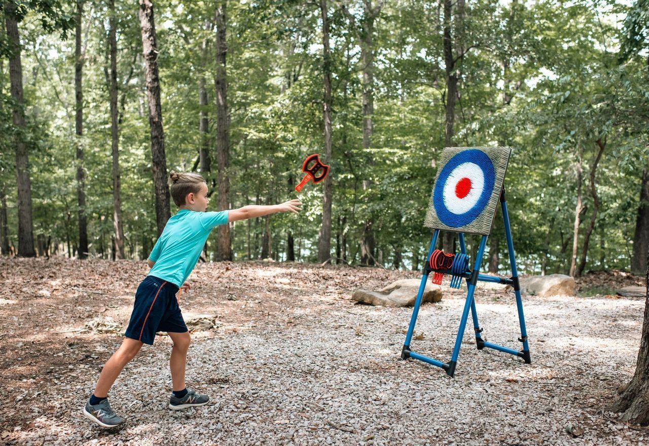 A young boy is throwing a frisbee at a target in the woods.