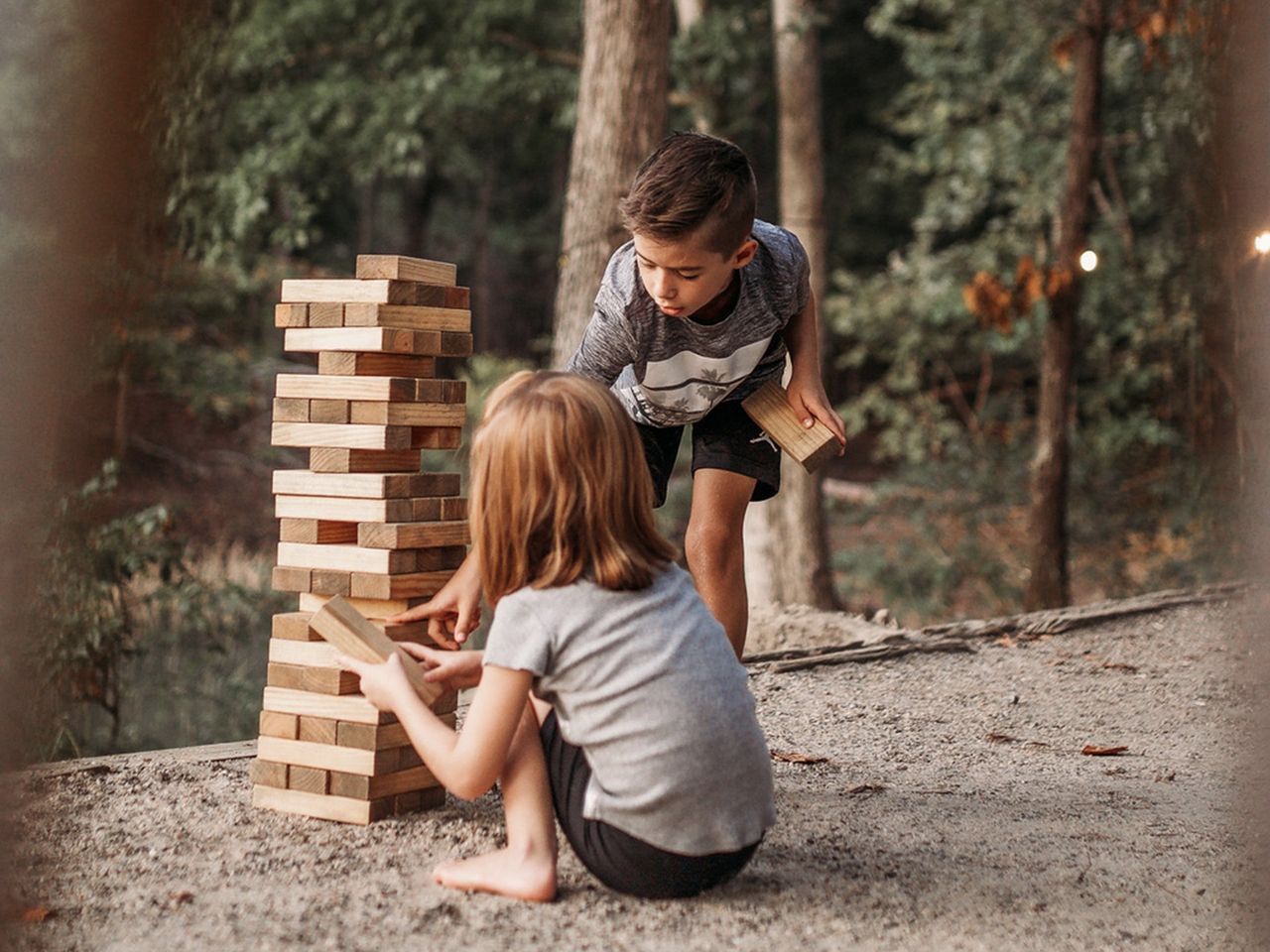 A boy and a girl are playing a game of jenga in the woods.