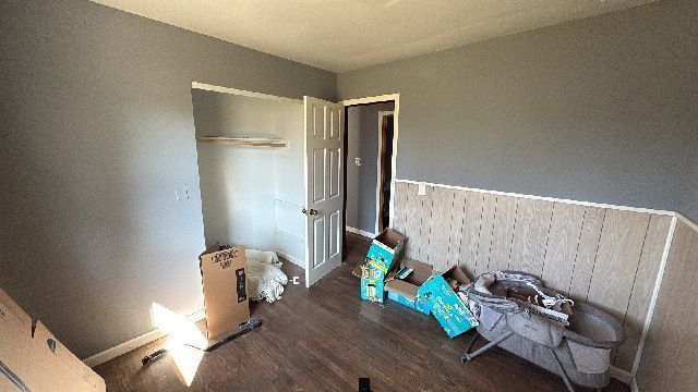 Empty bedroom with gray walls, wooden floors, closet, and baby items.