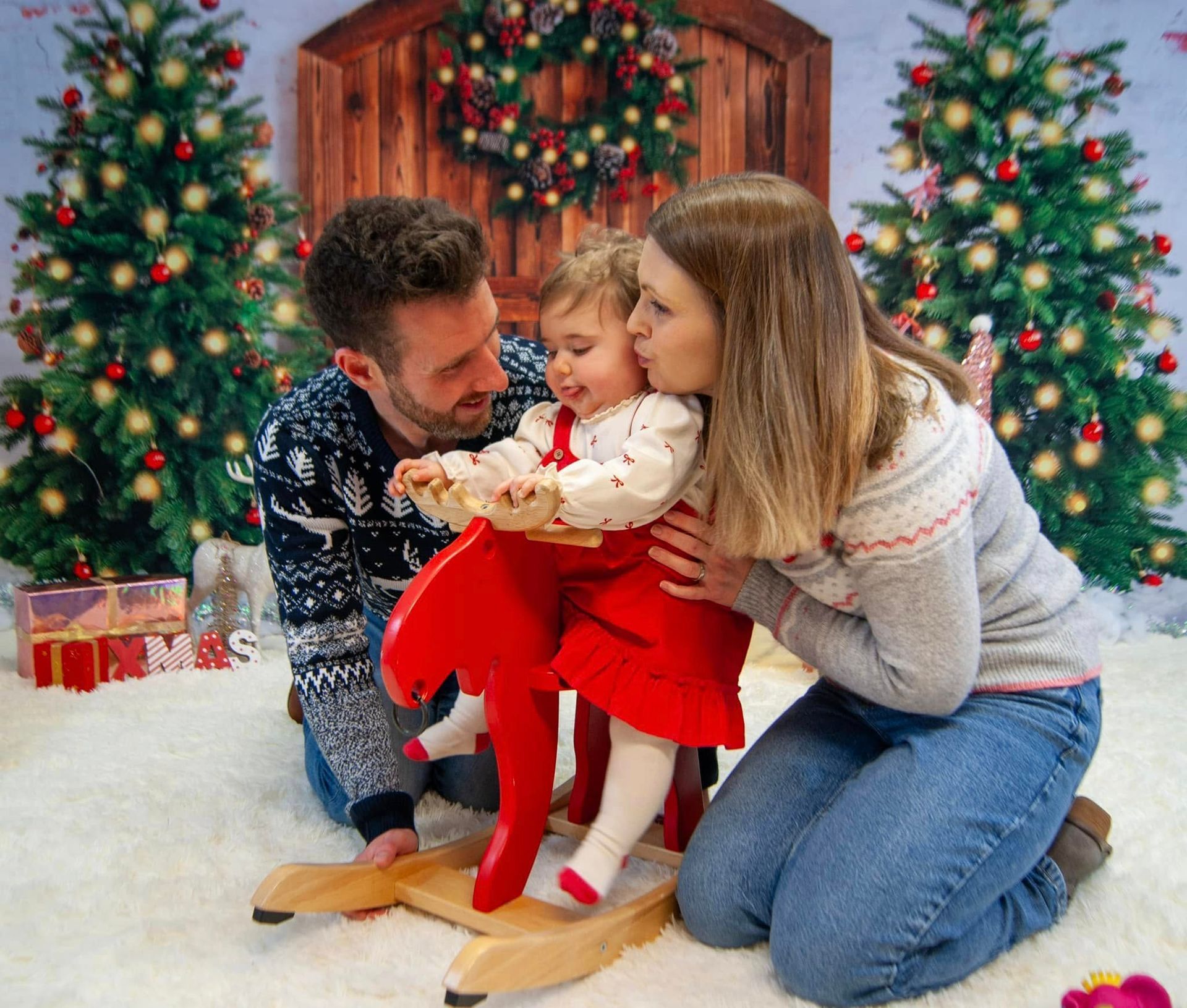 A family is posing for a picture with a baby on a rocking horse.