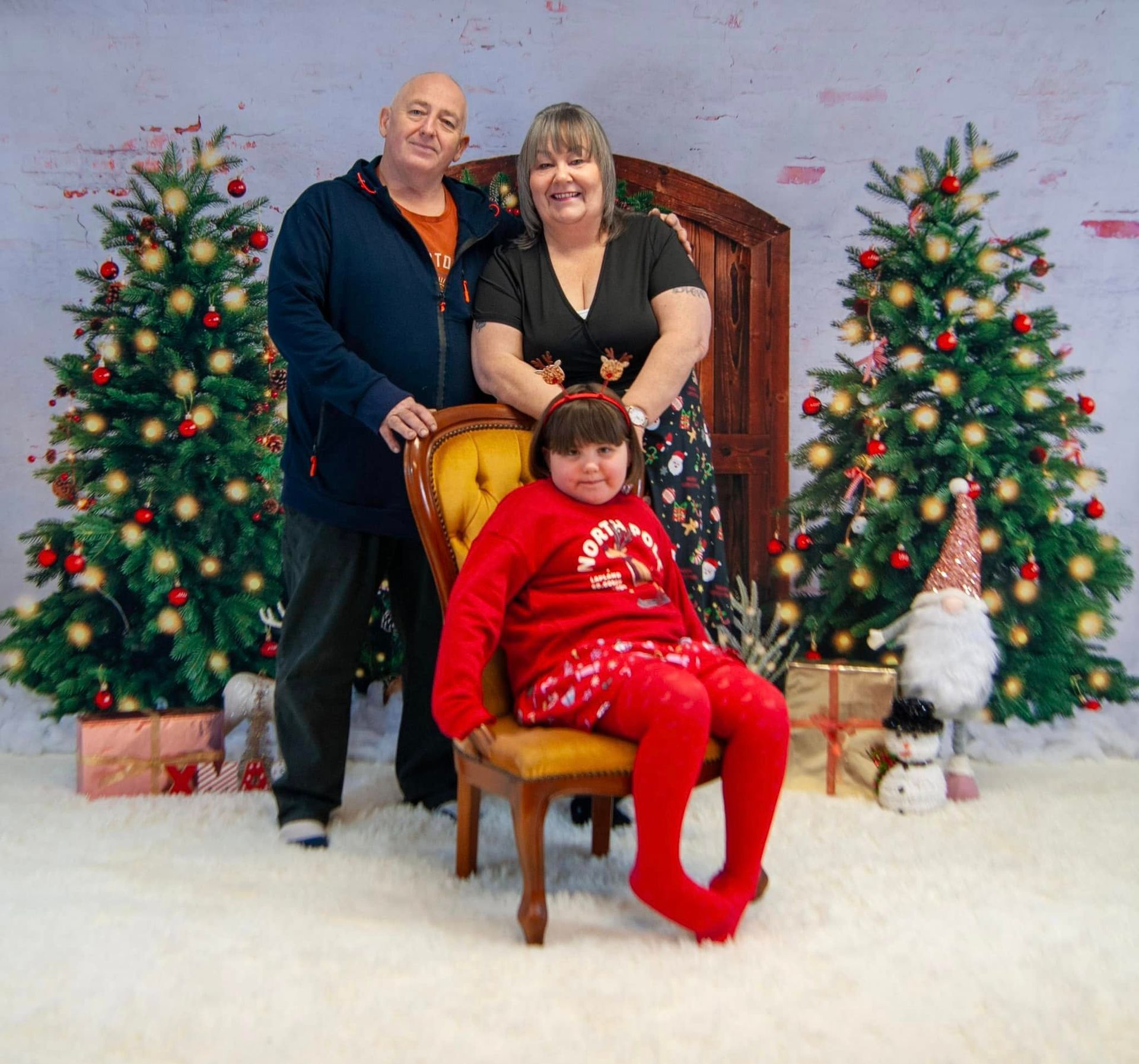 A family poses for a picture in front of christmas trees