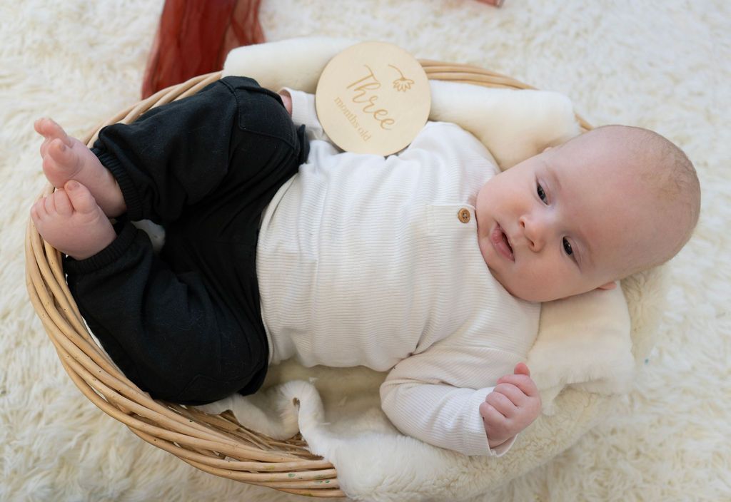 A baby is laying in a wicker basket on a blanket.