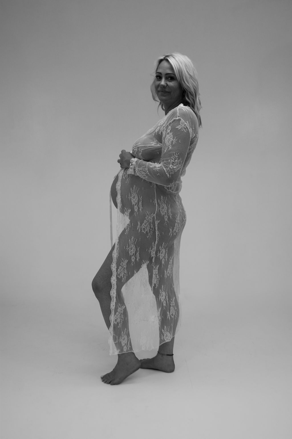 A black and white photo of a pregnant woman in a lace dress.