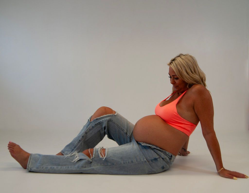 A pregnant woman is sitting on the floor with her legs crossed