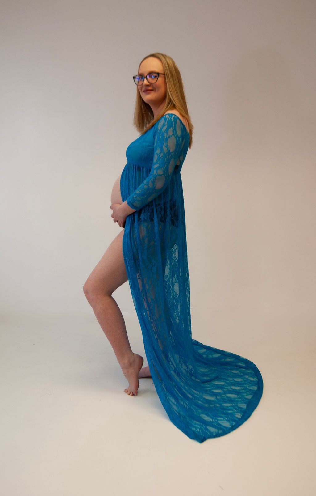 A pregnant woman is wearing a blue lace dress and glasses.
