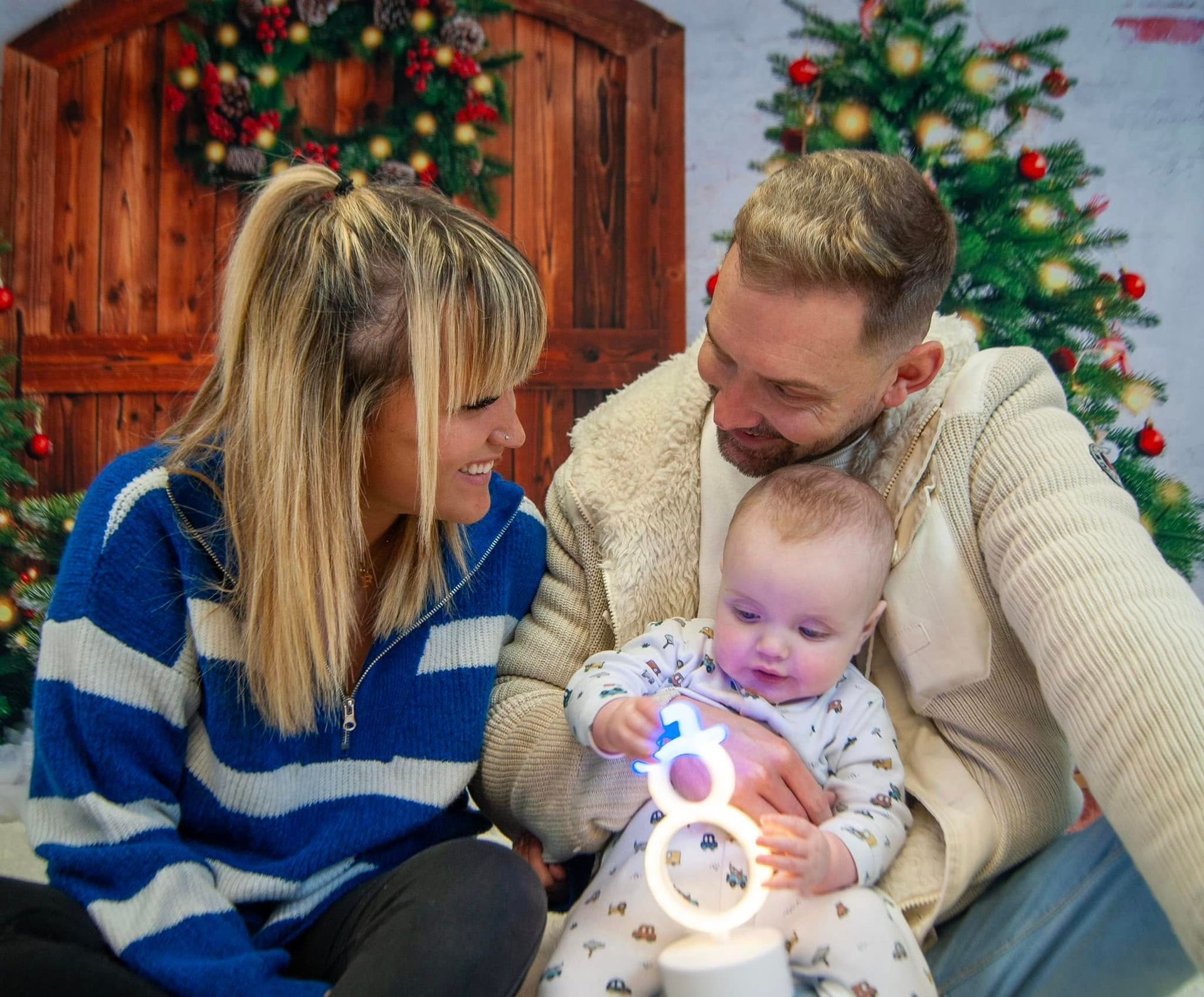 A man and woman are holding a baby in front of a christmas tree.