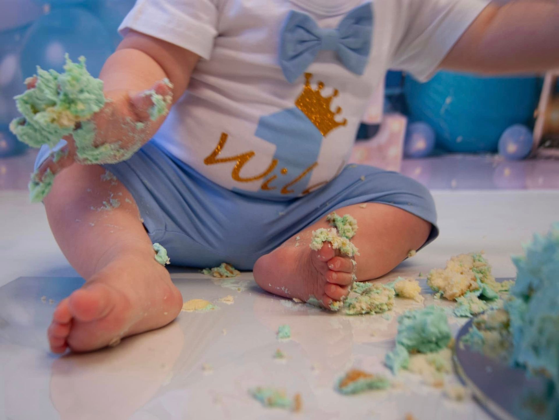 A baby is sitting on the floor covered in cake crumbs.