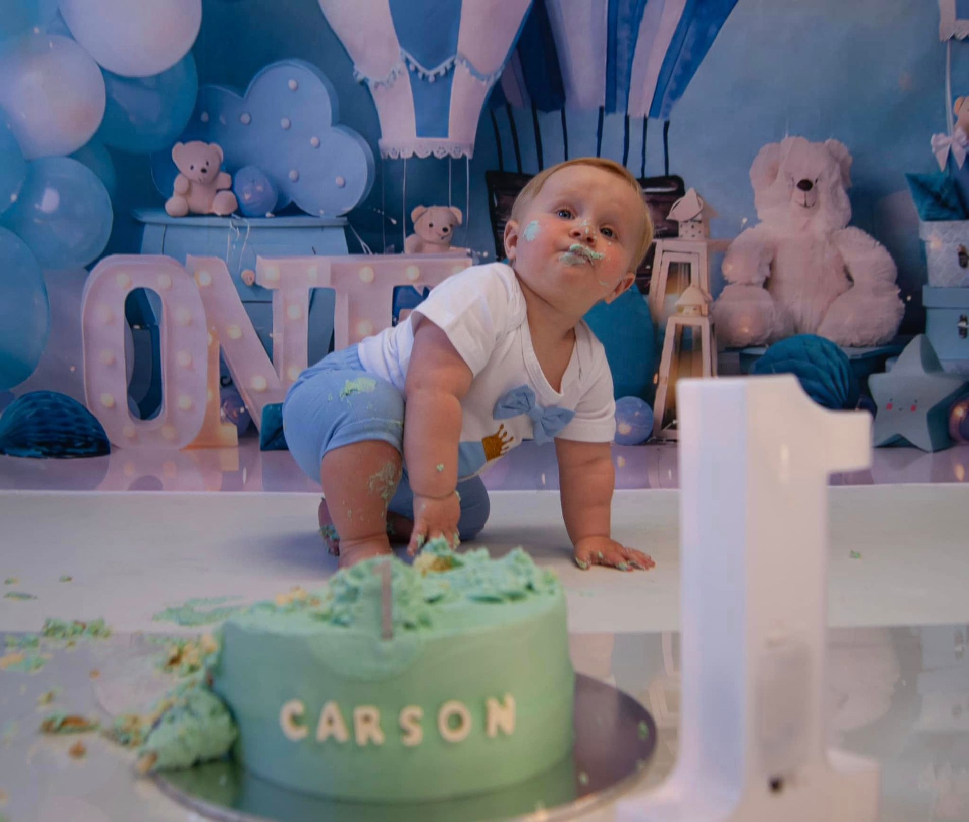 A baby is crawling on the floor next to a cake.