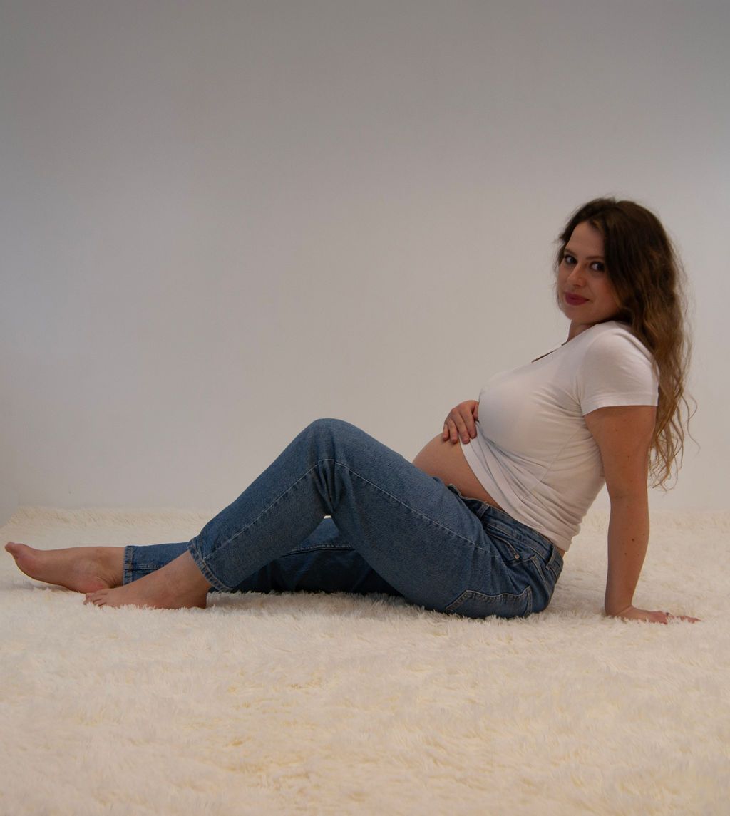 A pregnant woman is sitting on the floor with her legs crossed