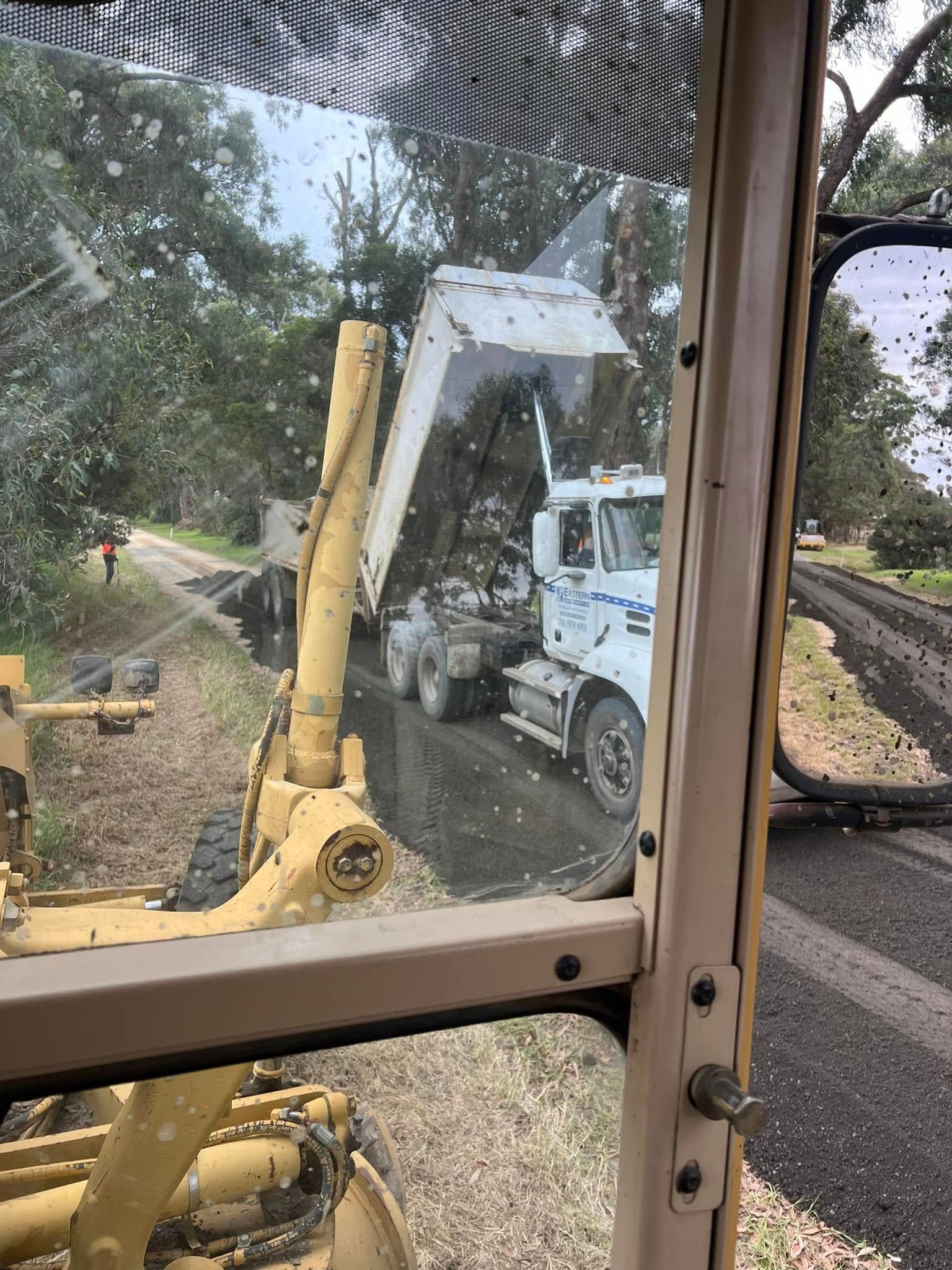 White truck and yellow excavator beside a rail line, seen through a window.