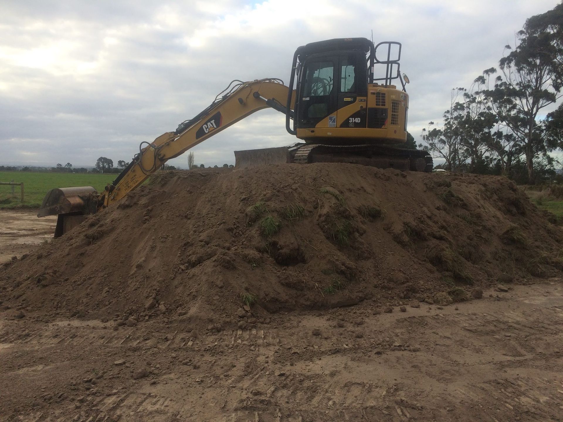 Excavator digging a dirt mound at sunset under a pink-orange sky