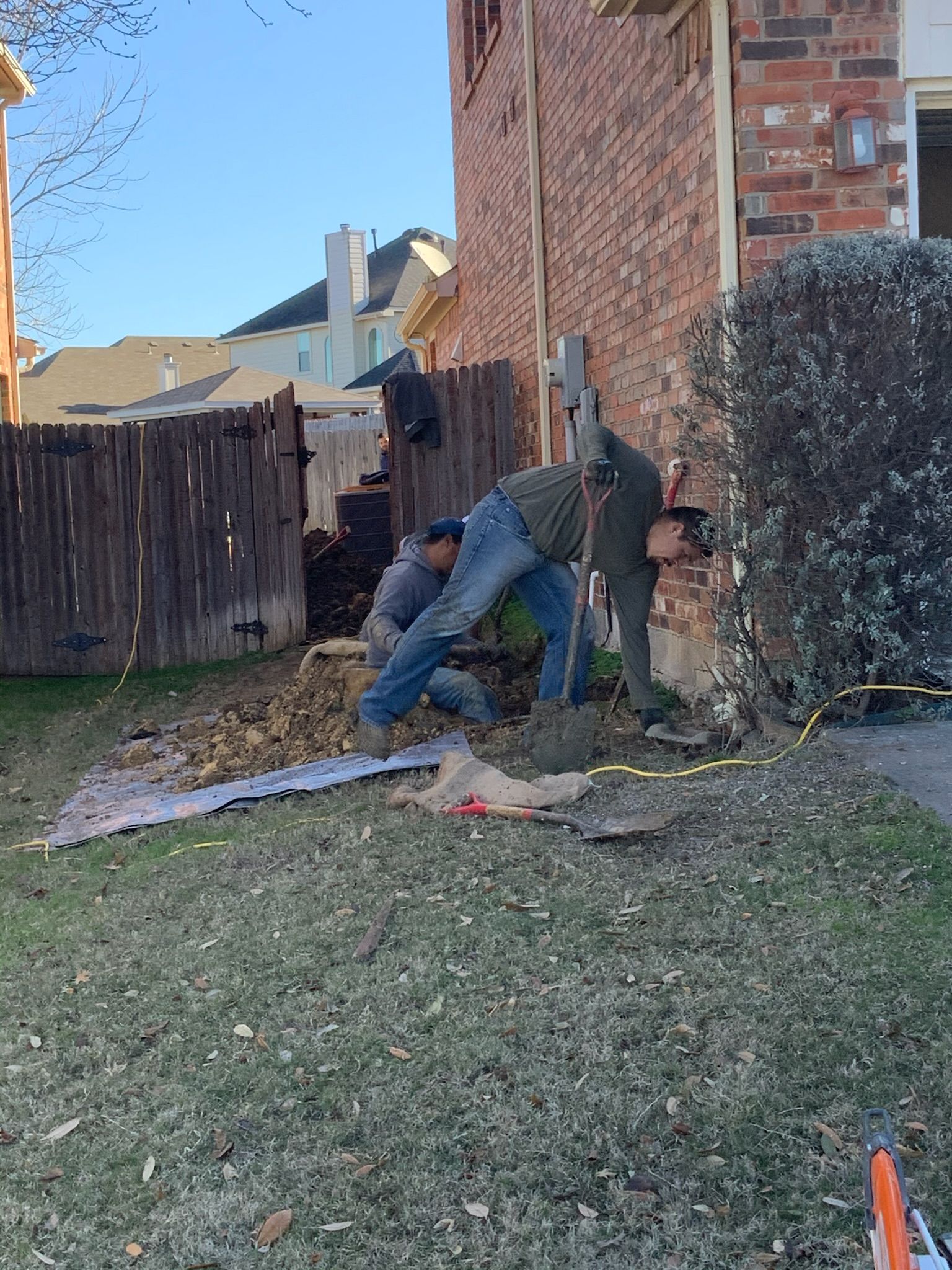 two men are digging in the dirt in front of a brick house