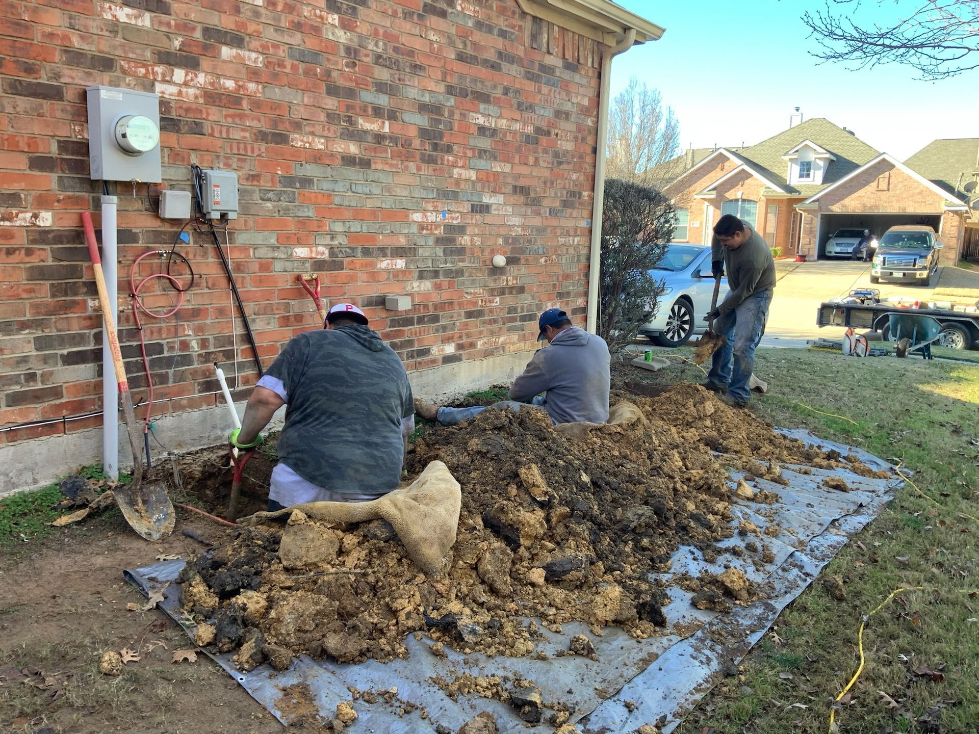 three men are digging a hole in front of a brick house
