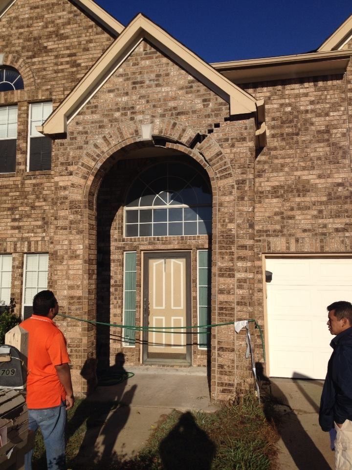 a man in an orange shirt stands in front of a brick house