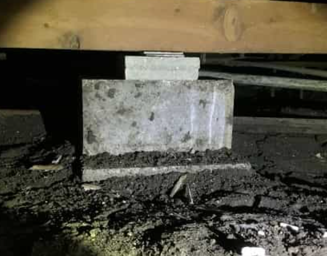 a concrete block is sitting on top of a pile of dirt under a wooden beam.