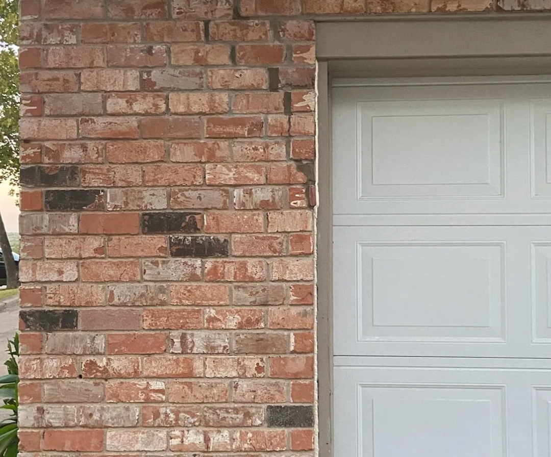a white garage door is next to a red brick wall