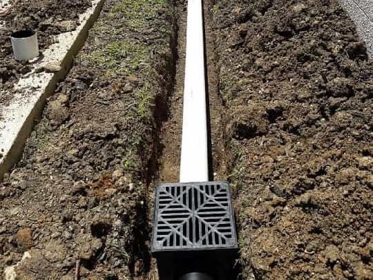 a drain pipe is being installed in a trench in the dirt .