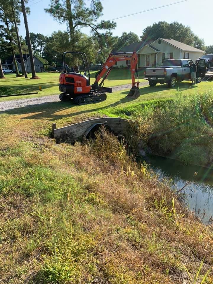 A small excavator is sitting in the grass next to a truck.