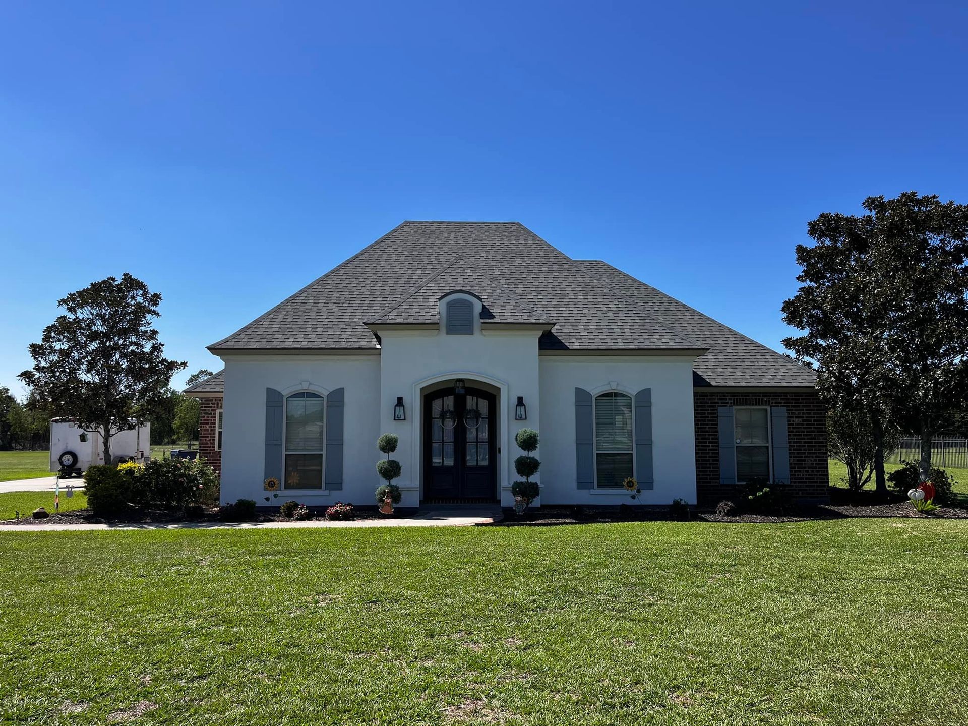 A white house with a roof and shutters is sitting on top of a lush green field.