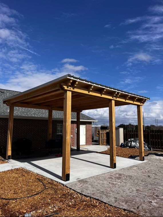 A wooden pergola is sitting in front of a brick house.