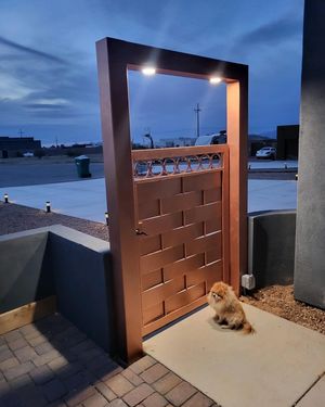 A small dog is sitting in front of a copper gate