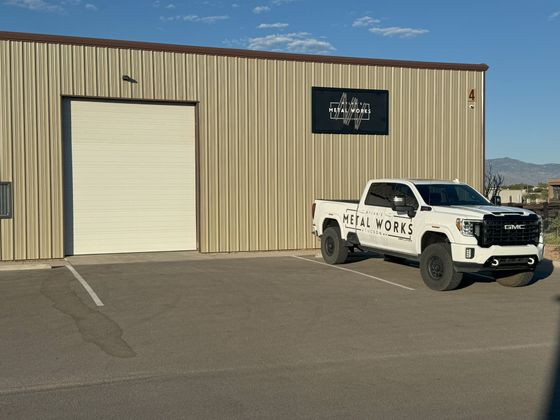 A white truck is parked in front of a metal building.