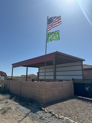 An american flag and a green flag are flying over a shed