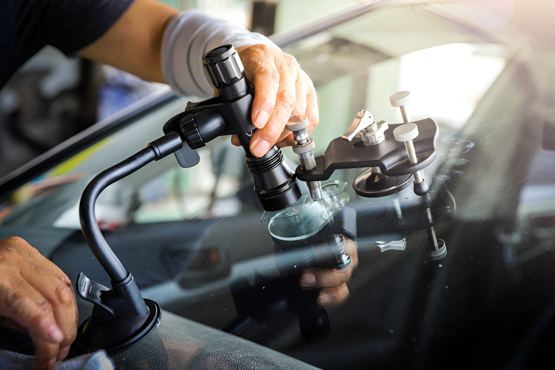 Technician repairing a car windscreen using a suction-mounted tool to fix a chip or crack.