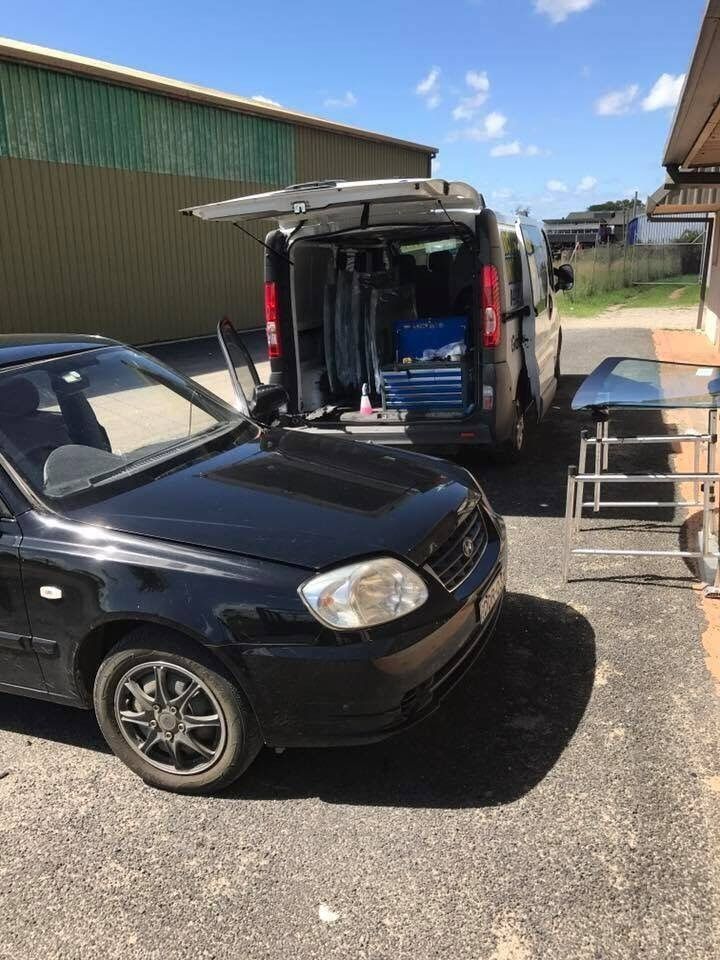 Black Car Parked Next to a Van With Open Back Doors, Outdoors on a Sunny Day — Road Runner Windscreens in Maclean, NSW