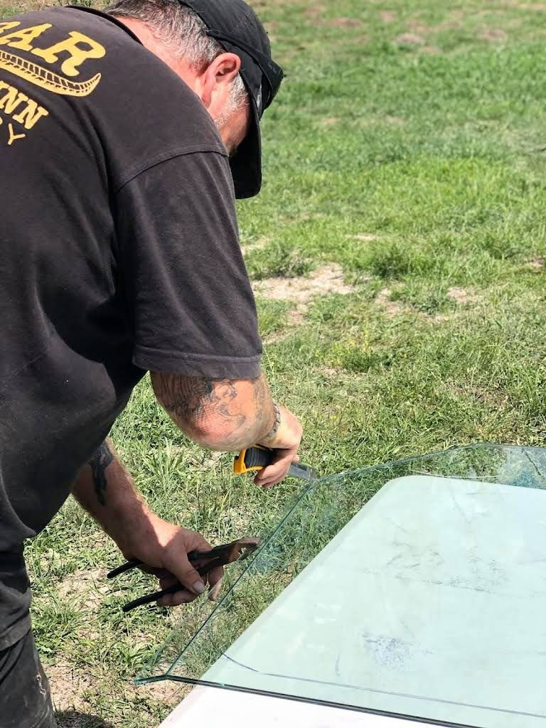 Man Cuts Wire Mesh on a Foam Board Outside, Wearing a Black T-shirt and Hat — Road Runner Windscreens in South Grafton, NSW