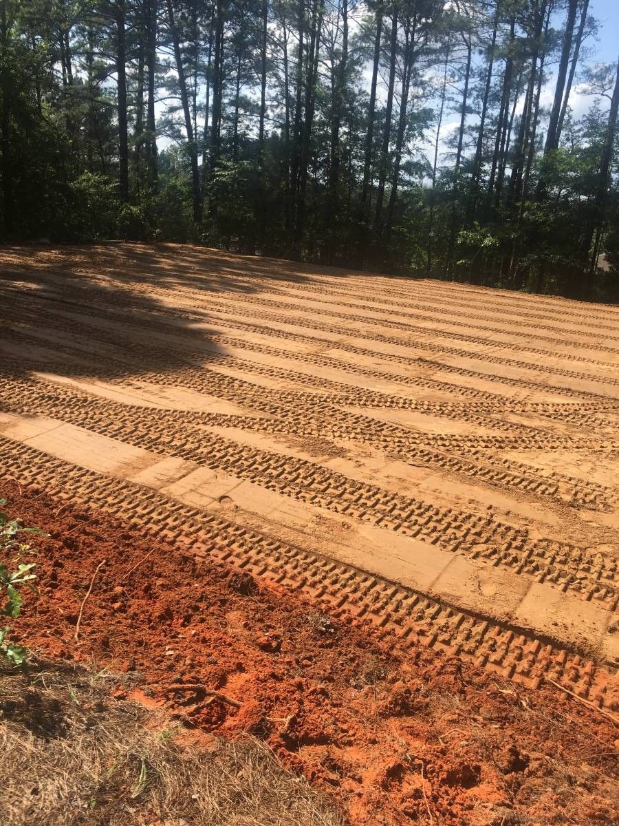 Freshly graded and leveled ground on a rural property surrounded by trees. 