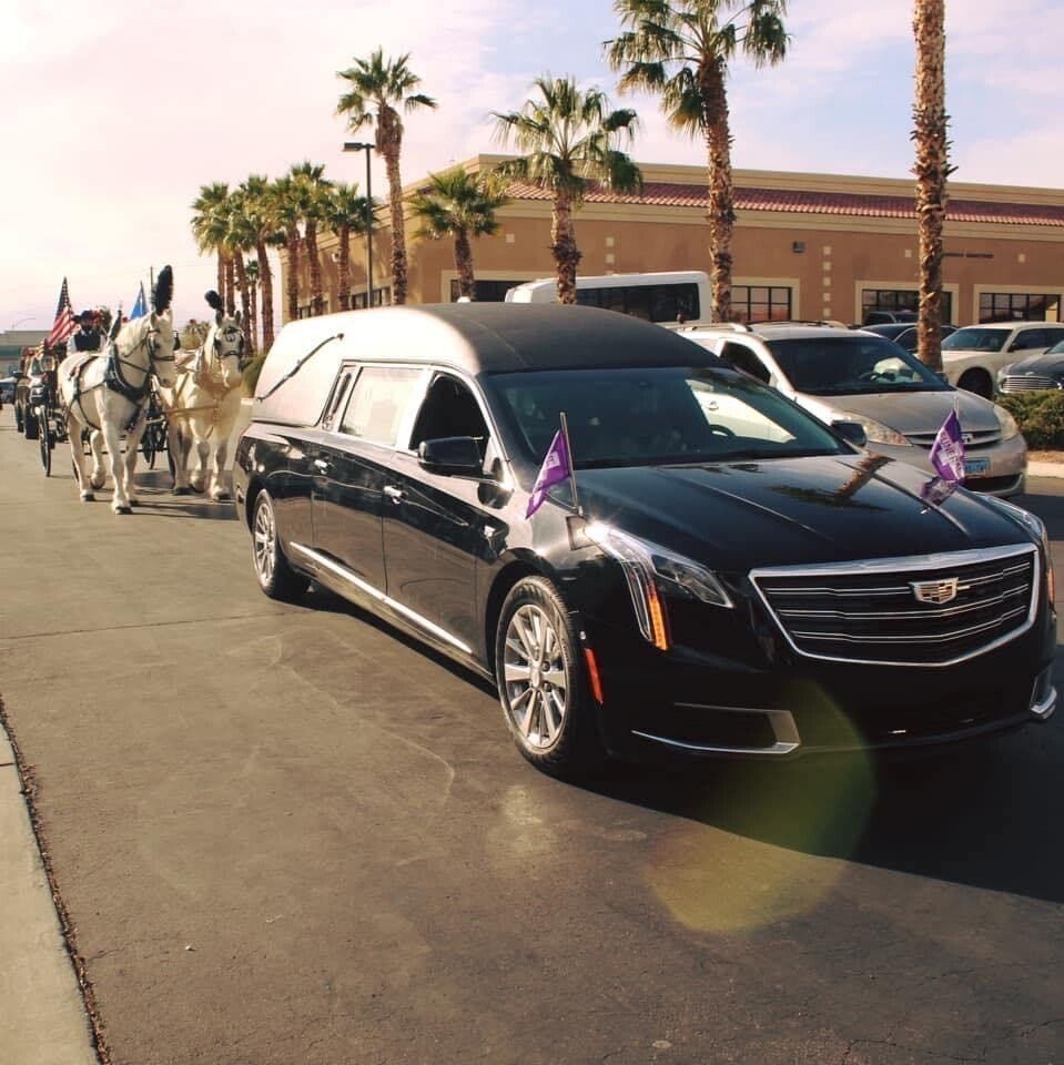 A horse drawn carriage pulls a black limousine down a street