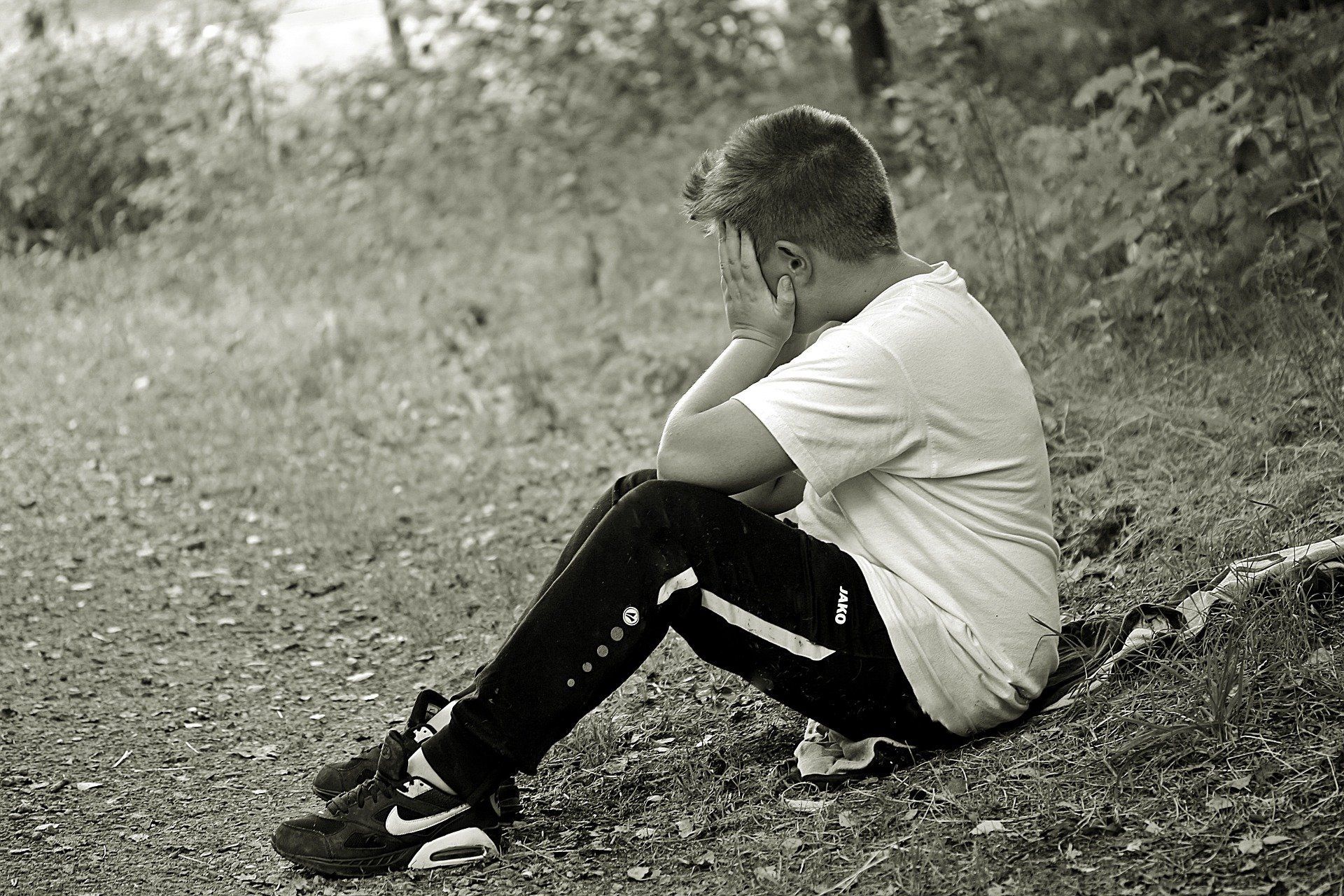 A young boy is sitting on the ground with his head in his hands.