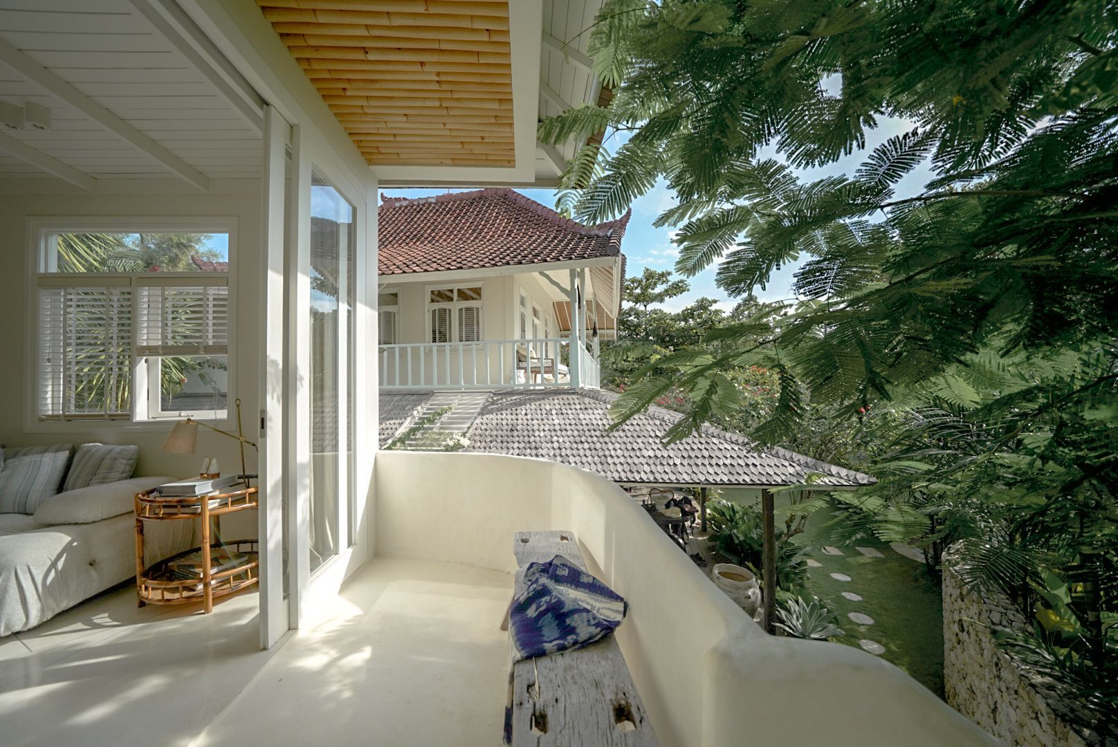 Balcony view of a white villa with lush greenery, including a glimpse of a tiled roof and exterior.