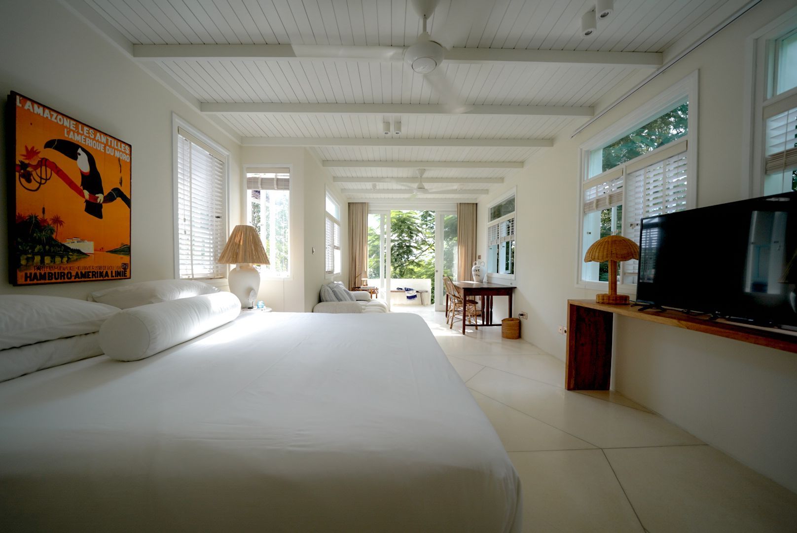 Bright, white bedroom with a large bed, a painting, windows, and a doorway leading outside.