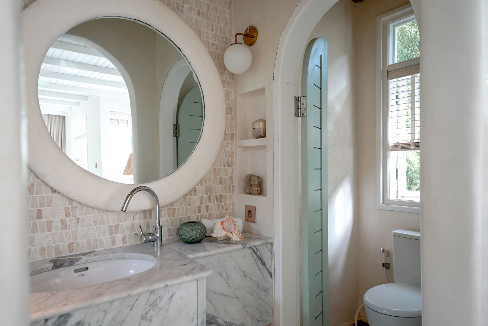 A bathroom with a circular mirror, marble countertop, and arched doorways in soft neutral tones.