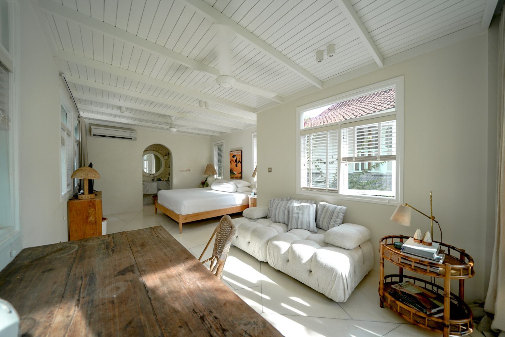 Bright white bedroom with a wooden table and sofa. A bed is visible in the background.