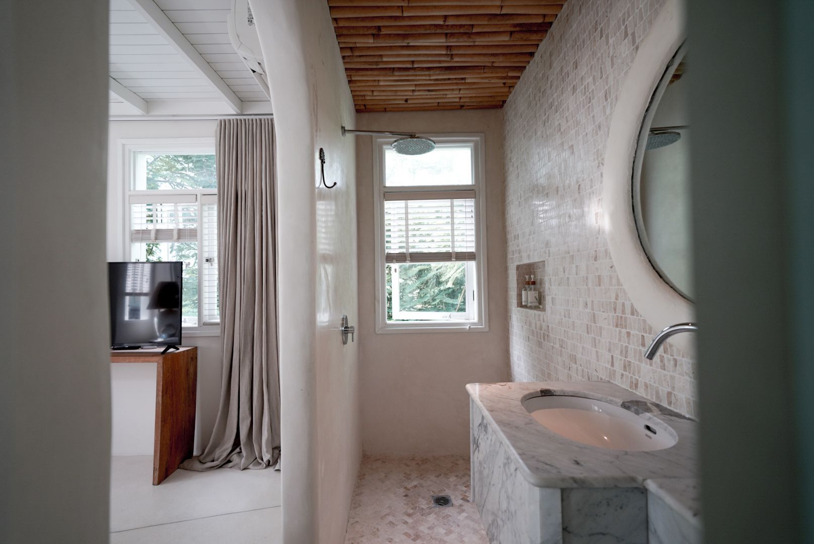 A bathroom with a marble sink, mosaic tile wall, and a window. The entrance to a bedroom is visible on the left.