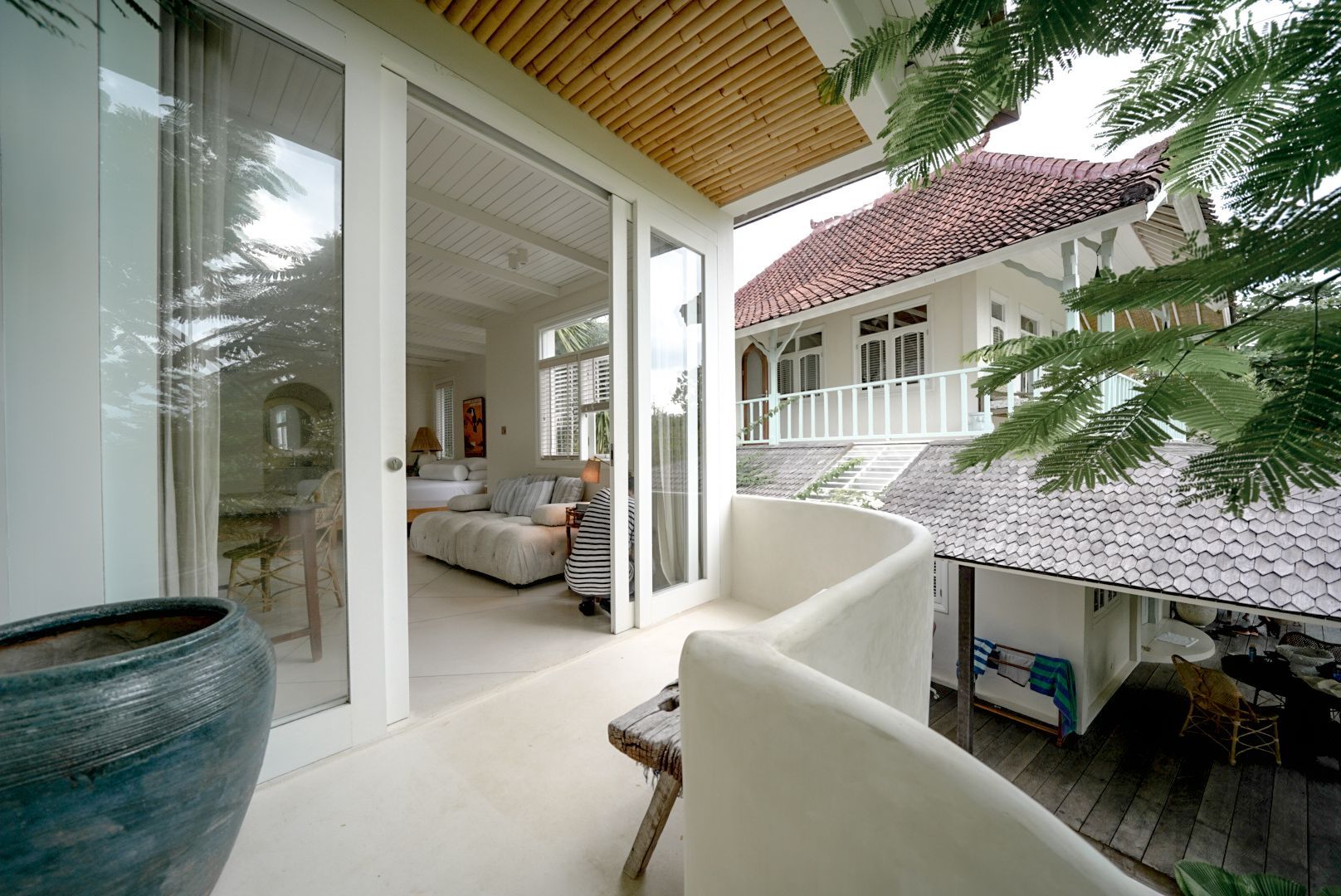 Balcony view of a white house with sliding glass doors, a curved wall, and a large pot, with another house in the background.