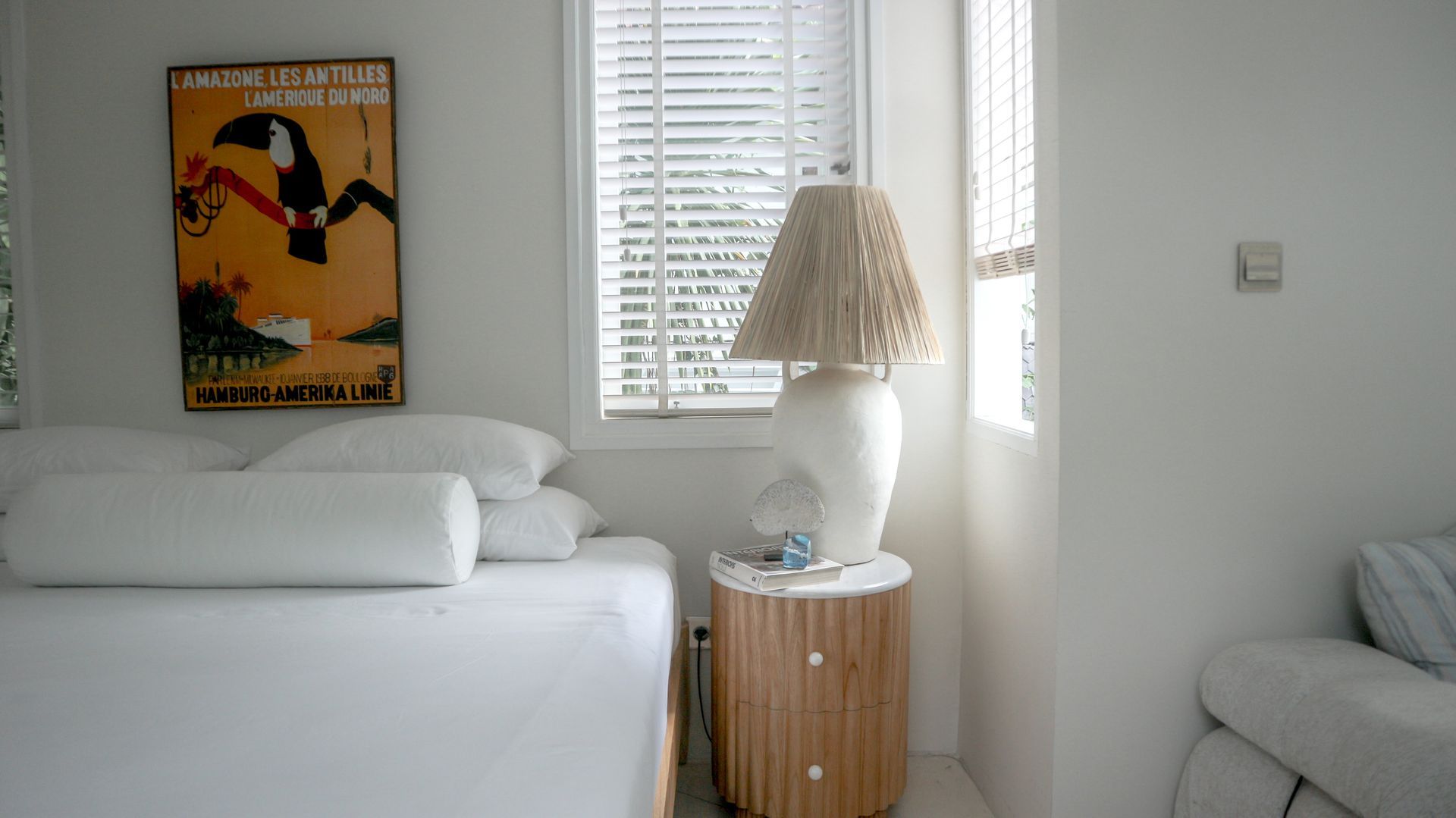 Bedroom corner with a bed and a side table. A lamp sits on the table, with a piece of art on the wall above the bed.