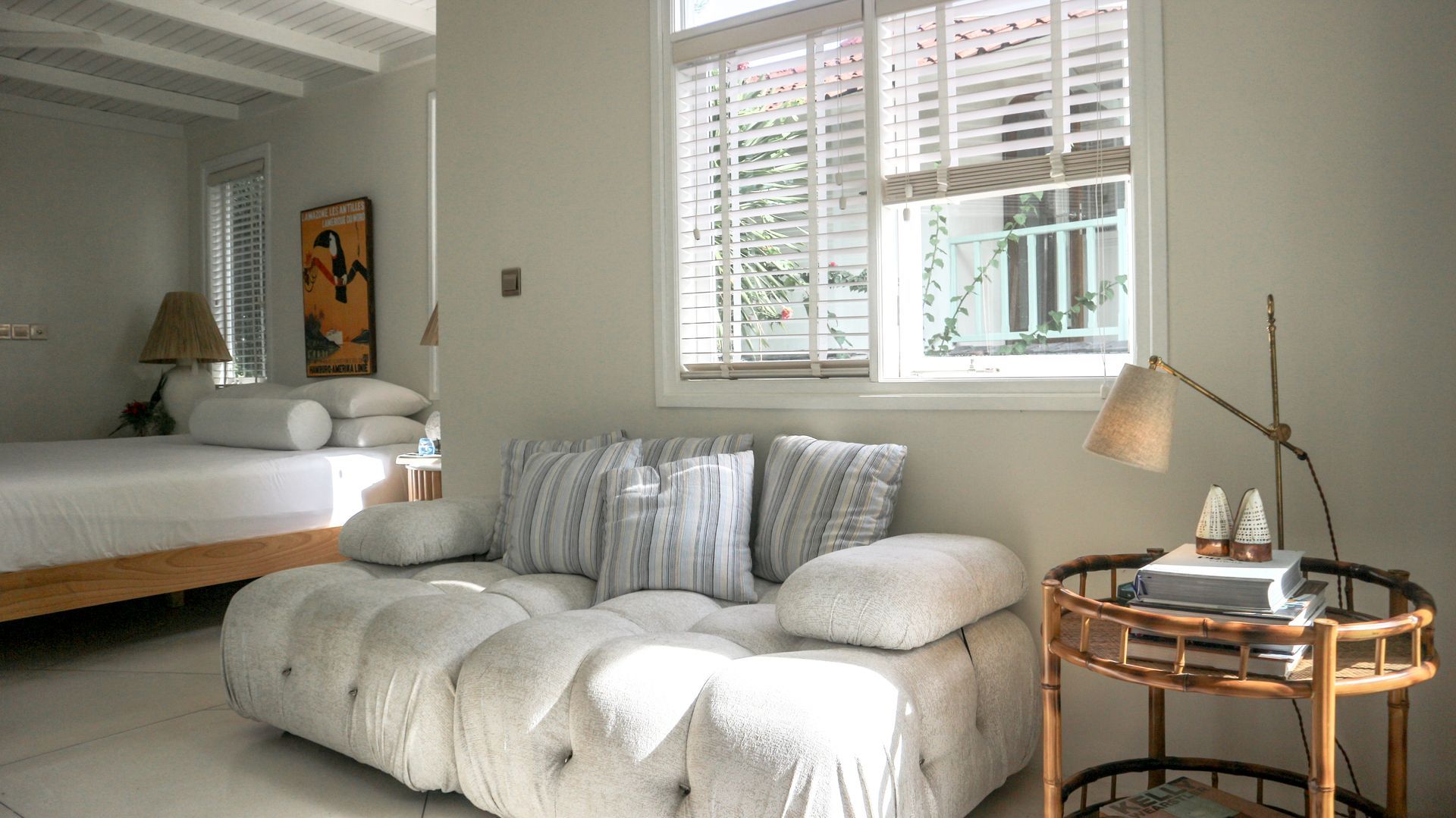 Cozy bedroom interior with a white tufted sofa, a wooden side table, and a bed. The room is bathed in natural light.