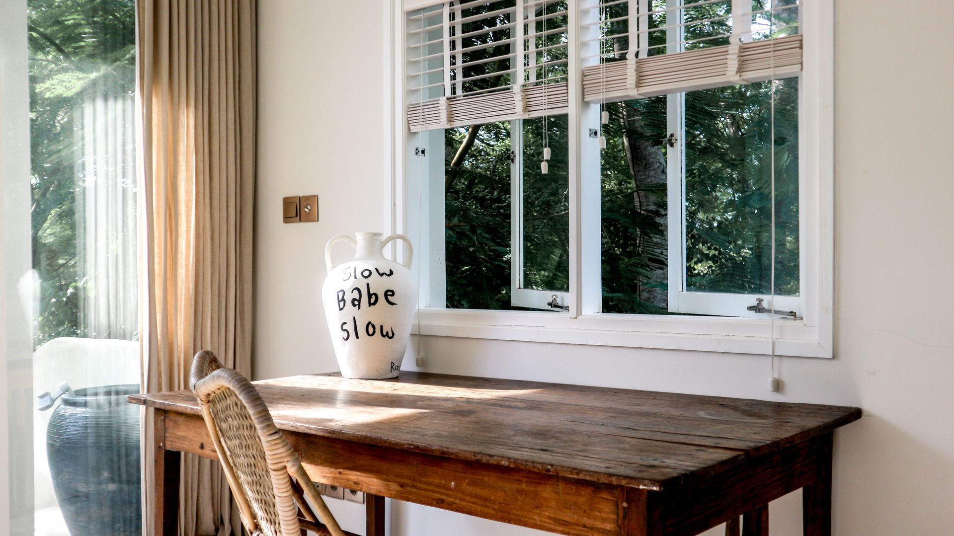 Wooden desk near a window with a white frame. A ceramic vase with 