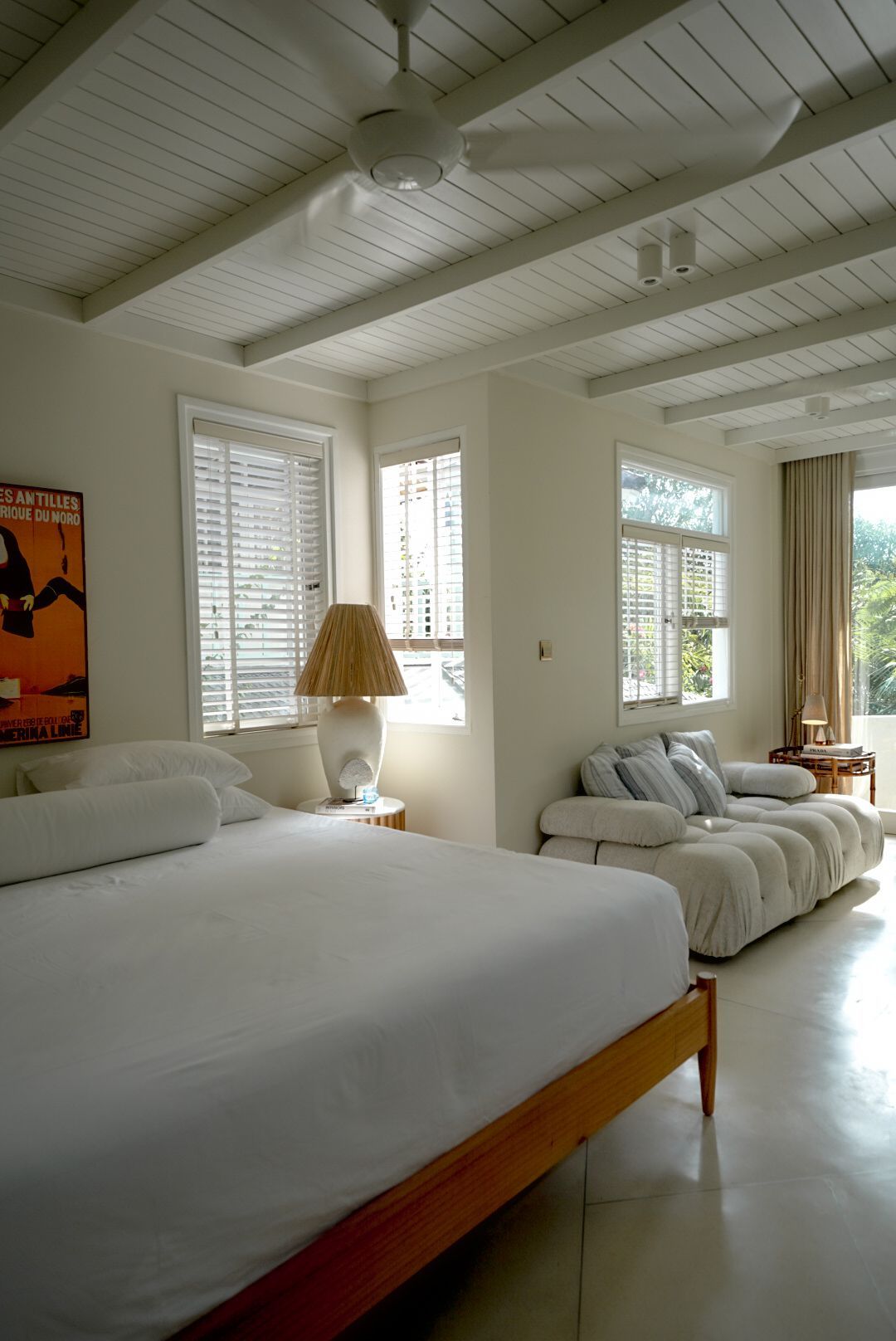 Bright bedroom with white ceiling beams, king-sized bed, and a sofa near windows with natural light.