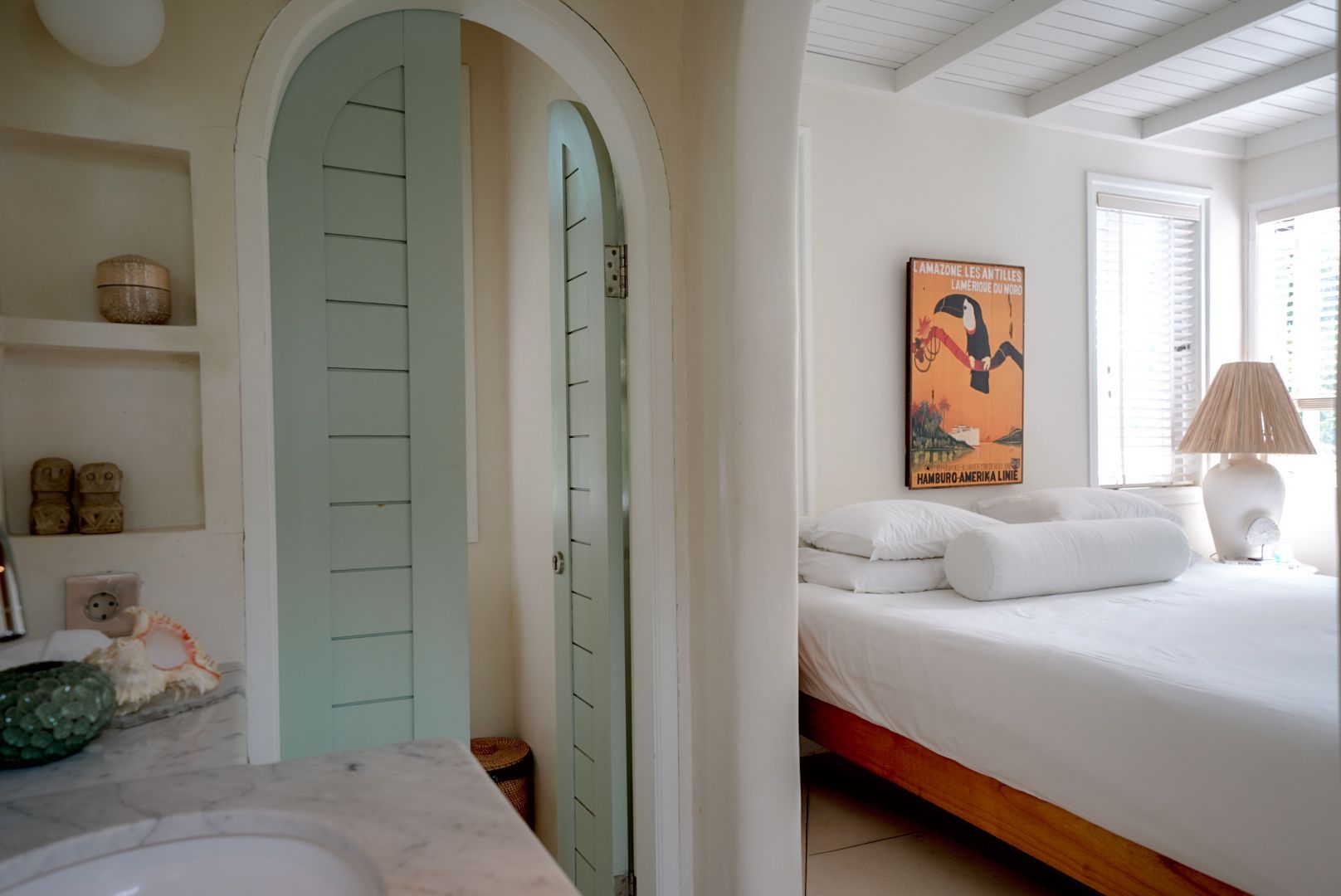 Bedroom with white bedding, a wooden bed frame, and a light-blue arched door leading to a bathroom with a marble sink.