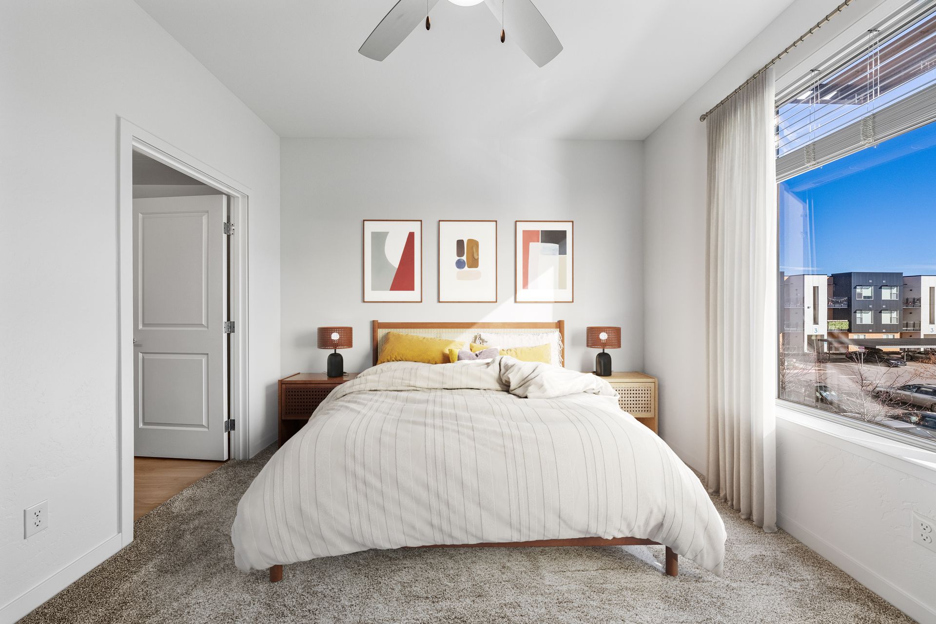 Bedroom in a modern apartment with a bed, two nightstands, and a large window.